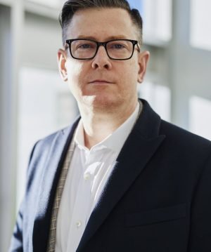 Profile portrait of a confident business executive wearing eyeglasses in a sunlit office setting.